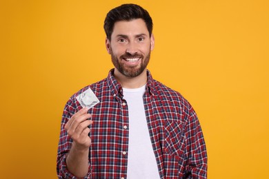 Photo of Happy man holding condom on yellow background, space for text. Safe sex
