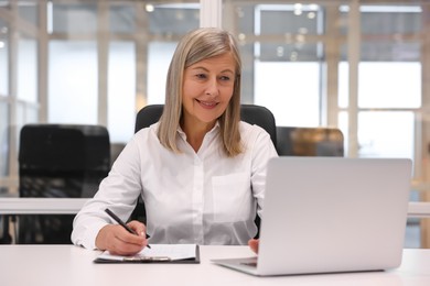 Photo of Smiling woman with clipboard and laptop working in office. Lawyer, businesswoman, accountant or manager