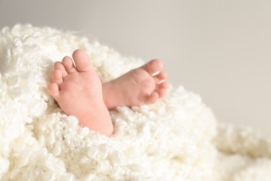 Little baby with cute feet wrapped in soft blanket against light background, closeup. Space for text