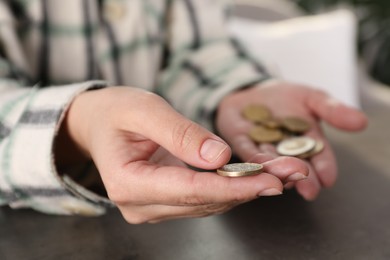 Photo of Poor woman holding coins at grey table indoors, closeup