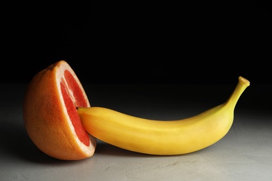 Photo of Fresh grapefruit and banana on table against black background. Sex concept
