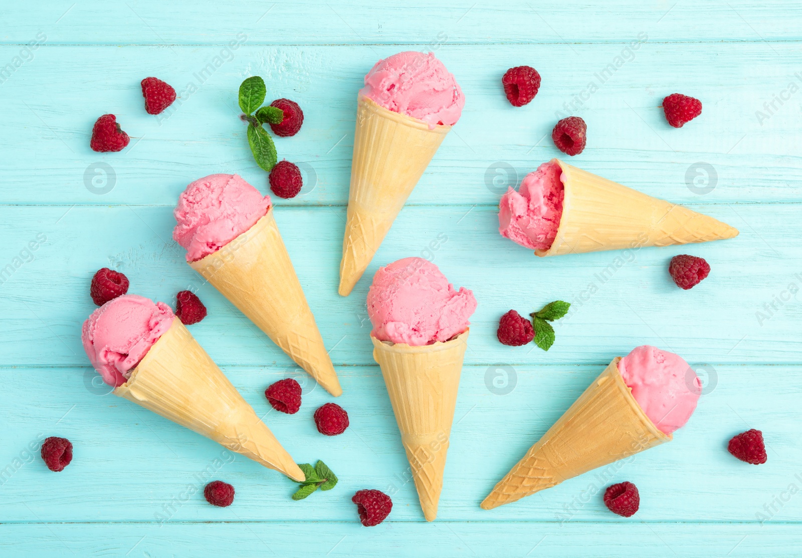 Photo of Flat lay composition with delicious pink ice cream in wafer cones and raspberries on light blue wooden table, flat lay