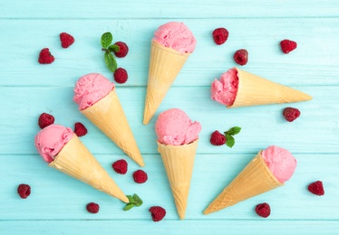 Photo of Flat lay composition with delicious pink ice cream in wafer cones and raspberries on light blue wooden table, flat lay