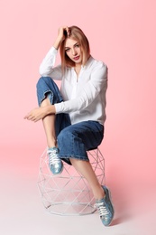 Fashionable young woman in stylish shoes on stool against color background