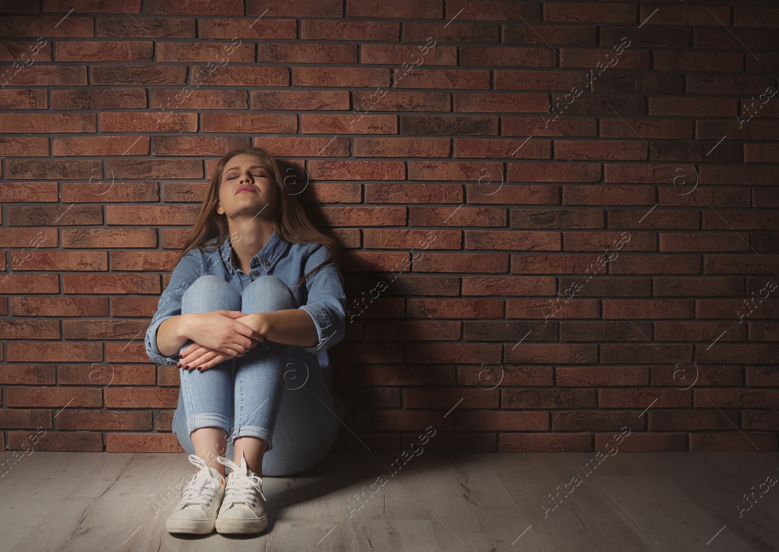 Photo of Depressed young woman sitting on floor near brick wall