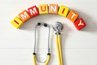 Photo of Colorful cubes with word Immunity and stethoscope on white wooden table, flat lay