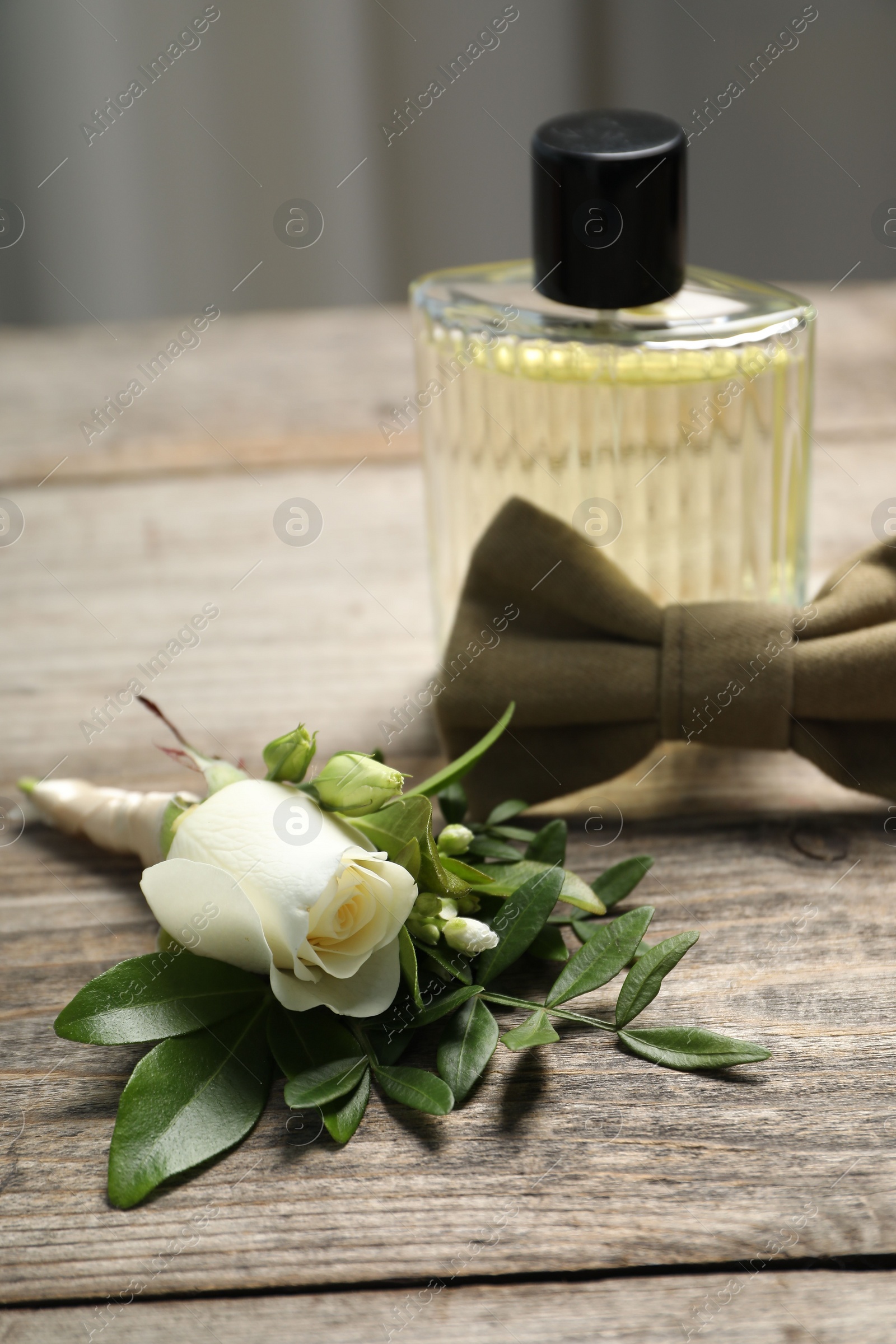 Photo of Wedding stuff. Stylish boutonniere, perfume and bow tie on wooden table, closeup