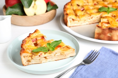 Slice of traditional apple pie with mint on white wooden table