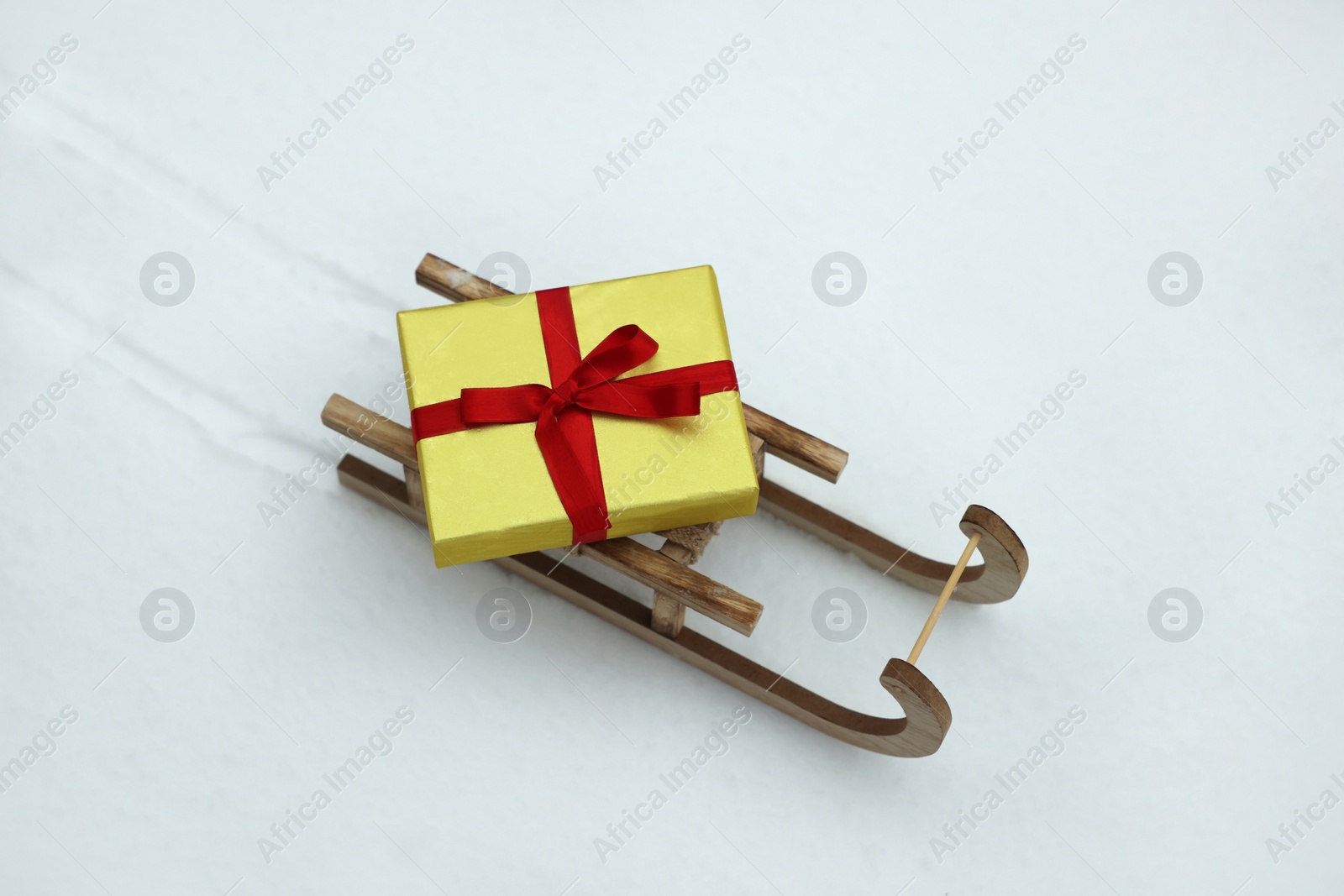 Photo of Wooden sleigh with gift box on snow outdoors, above view