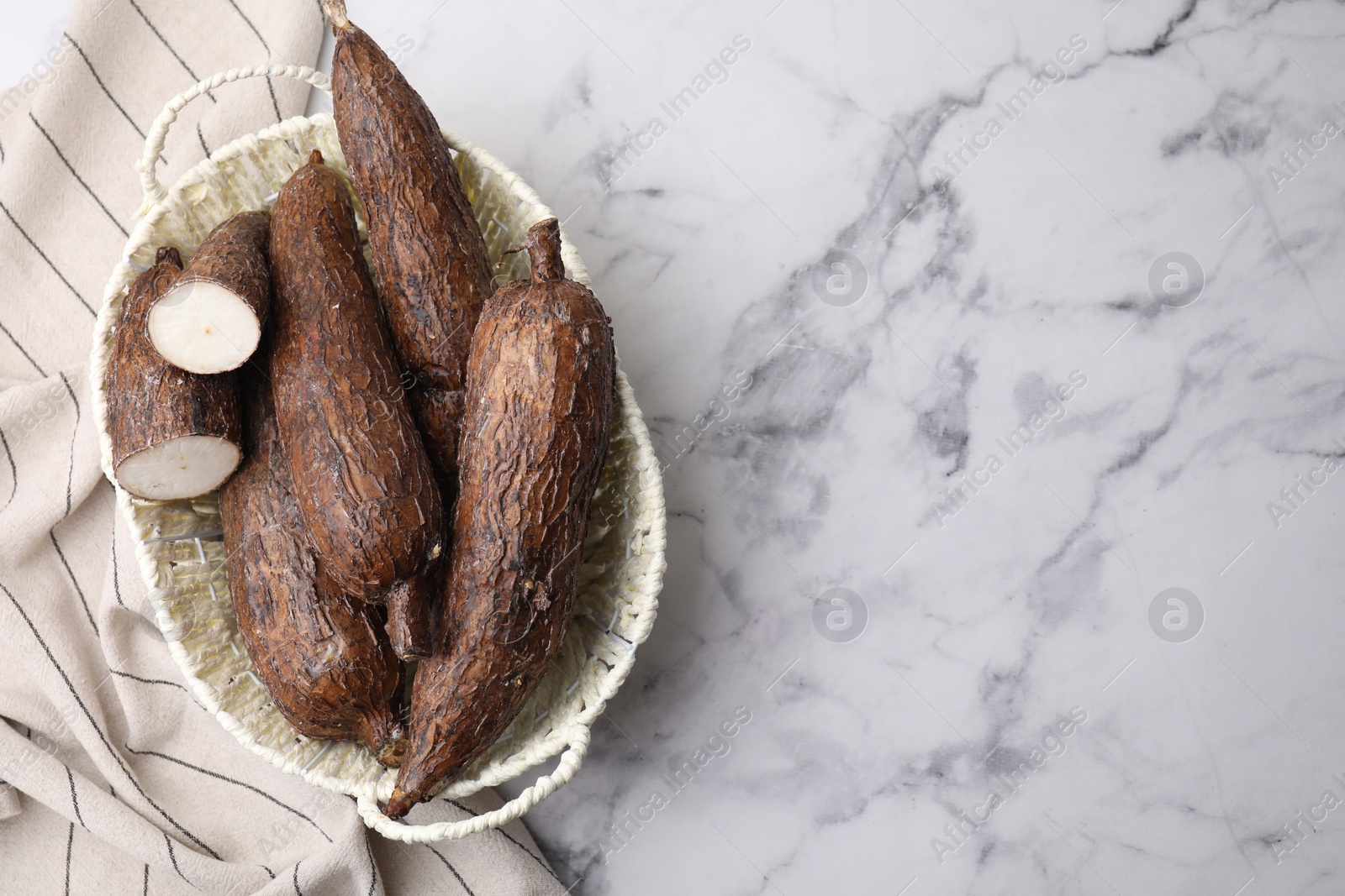 Photo of Whole and cut cassava roots in basket on white marble table, top view. Space for text