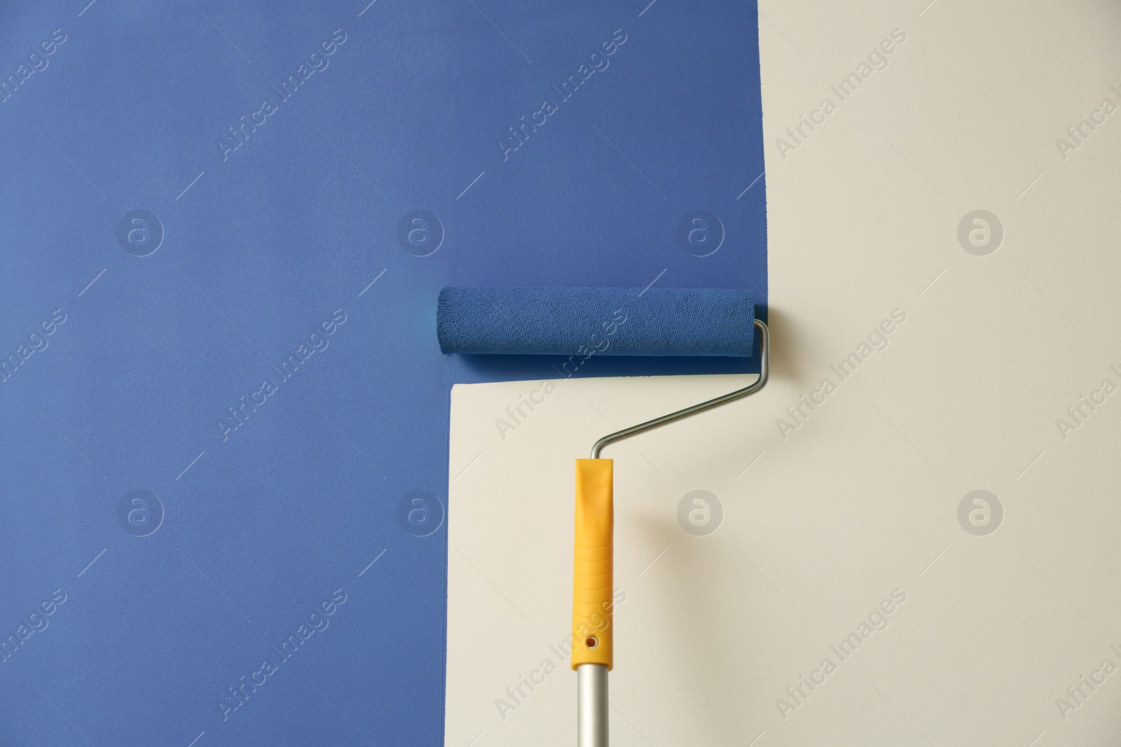 Photo of Applying green paint with roller brush on white wall