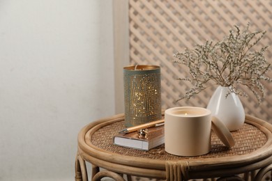 Photo of Burning soy candle, notebook and stylish accessories on wicker table indoors. Space for text