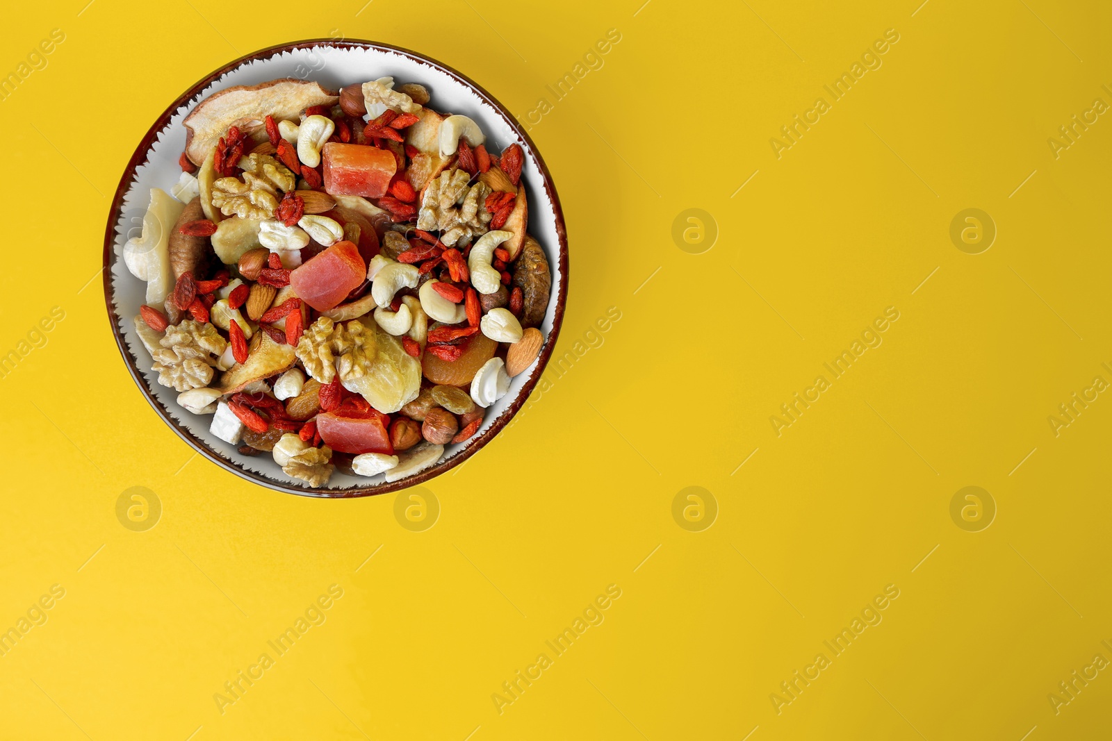 Photo of Bowl with mixed dried fruits and nuts on yellow background, top view. Space for text