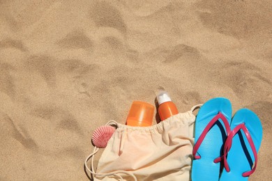 Sunscreens, seashell and beach accessories on sand, flat lay. Space for text