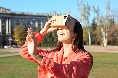 Photo of Young woman using cardboard virtual reality headset outdoors