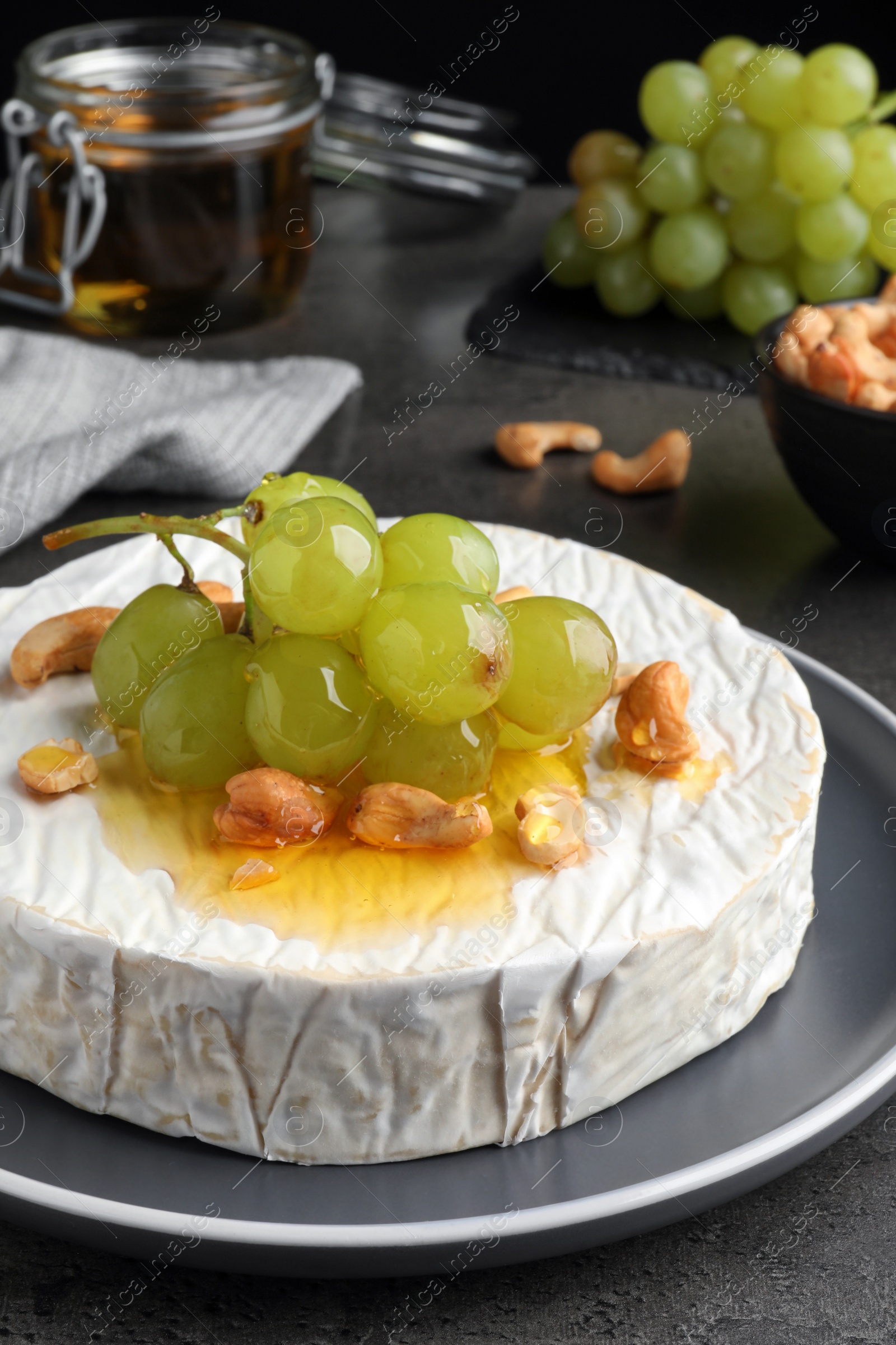 Photo of Brie cheese served with grape, cashew nuts and honey on dark grey table, closeup