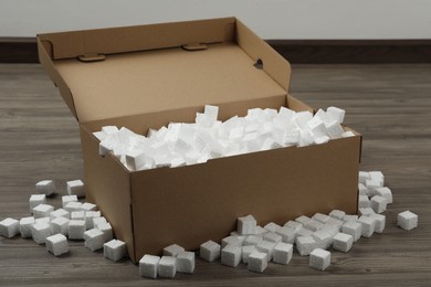 Photo of Cardboard box and styrofoam cubes on wooden floor indoors