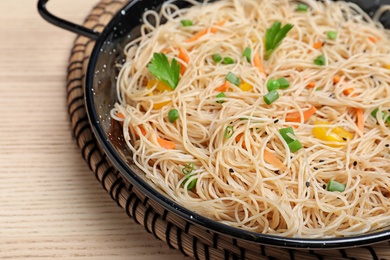 Pan with delicious asian noodles and vegetables on wooden background, closeup