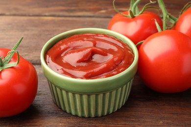 Photo of Bowl of tasty ketchup and tomatoes on wooden table, closeup