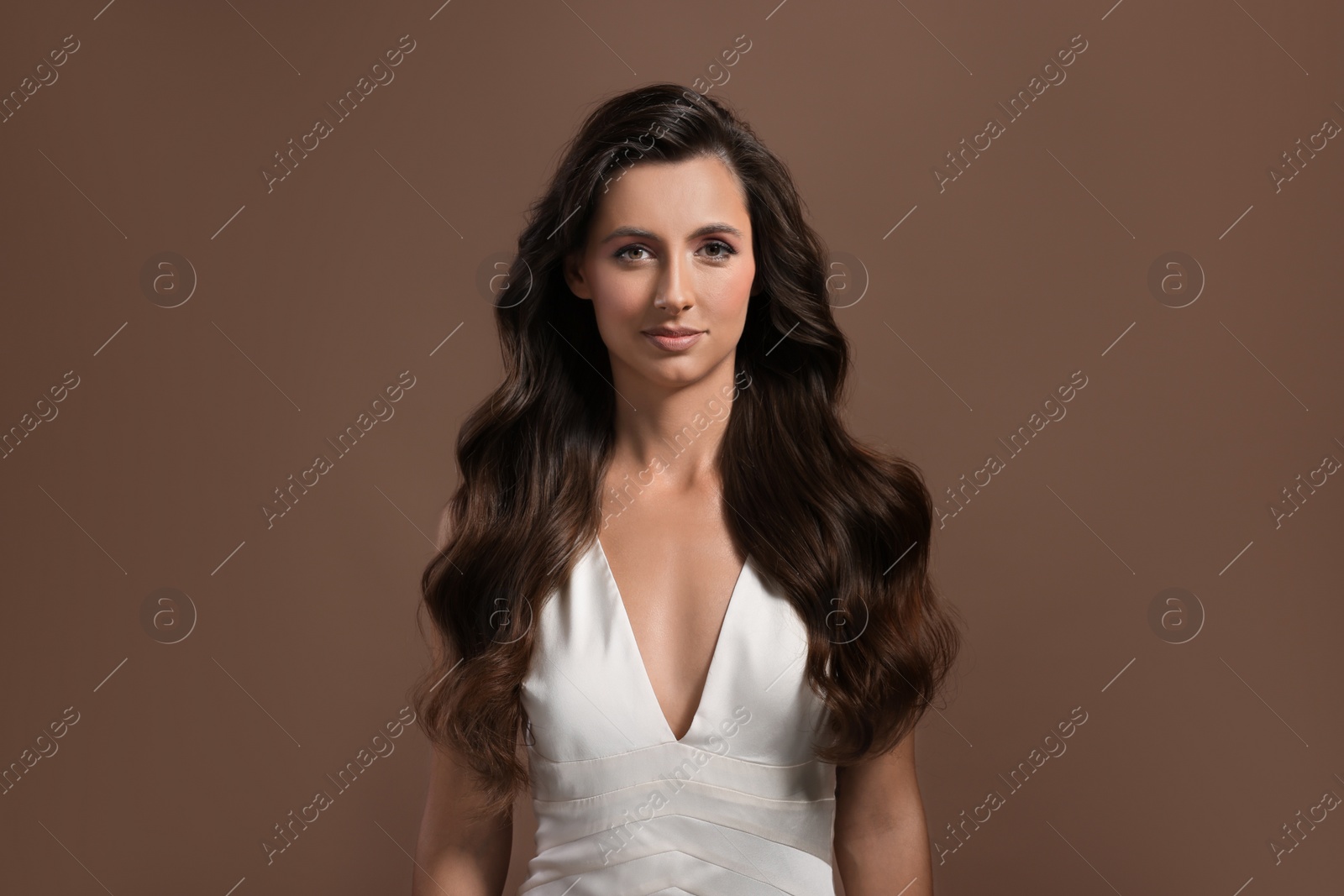 Photo of Hair styling. Portrait of beautiful woman with wavy long hair on brown background