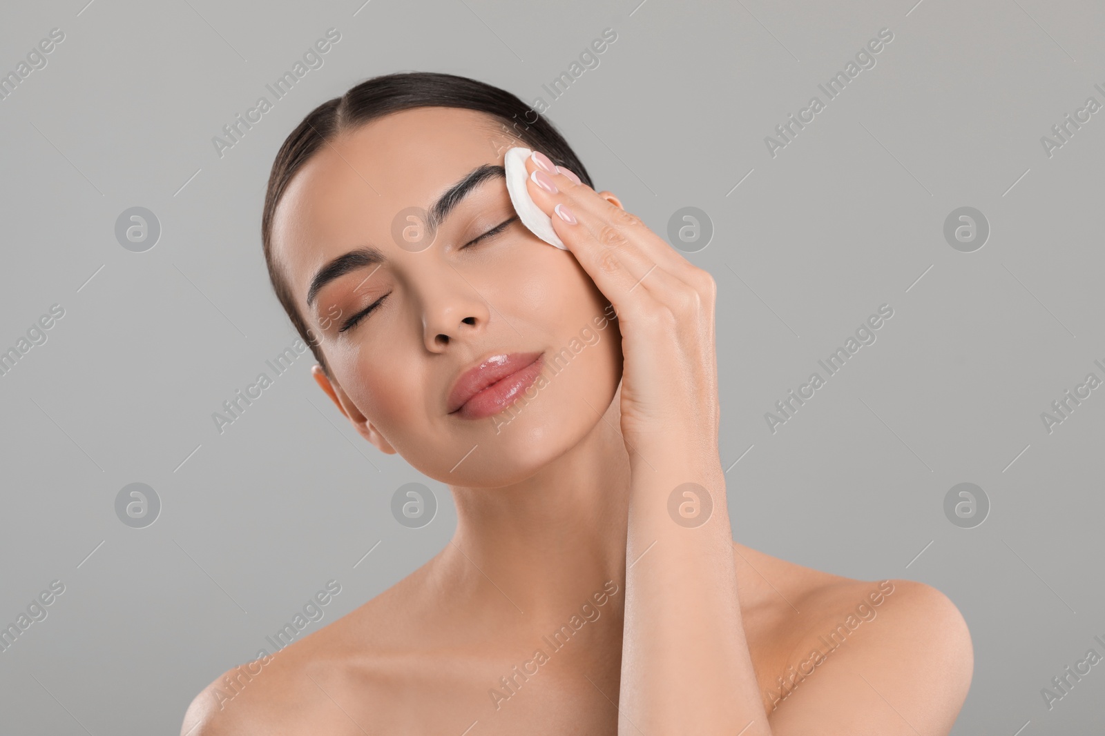 Photo of Beautiful woman removing makeup with cotton pad on light grey background