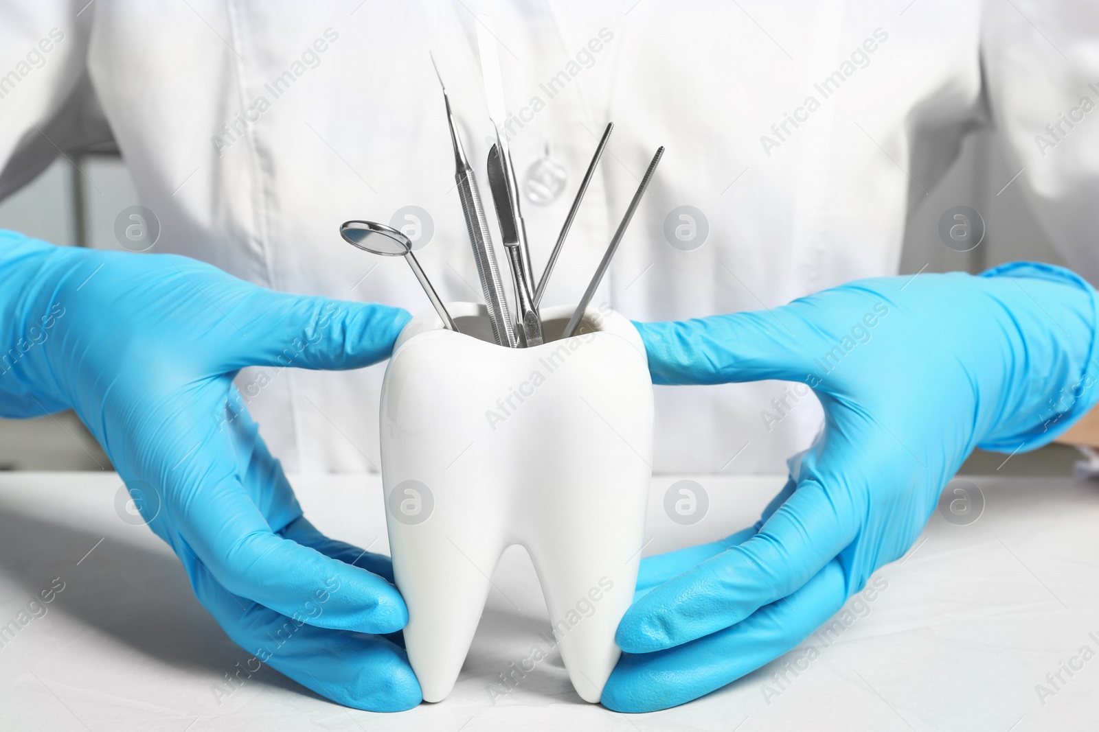 Photo of Dentist with tooth shaped holder full of professional tools at table, closeup