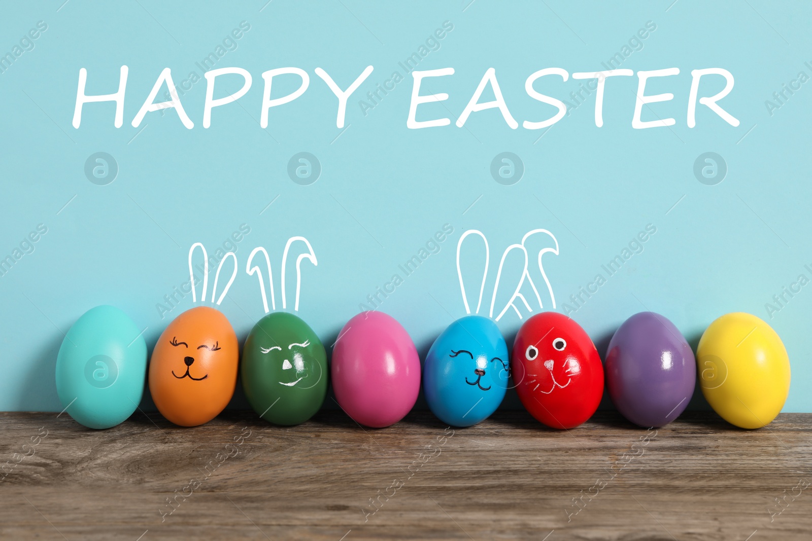 Image of Several eggs with drawn faces and ears as Easter bunnies among others on wooden table against light blue background