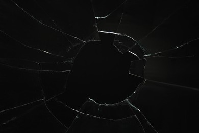 Photo of Closeup view of broken glass with cracks on black background