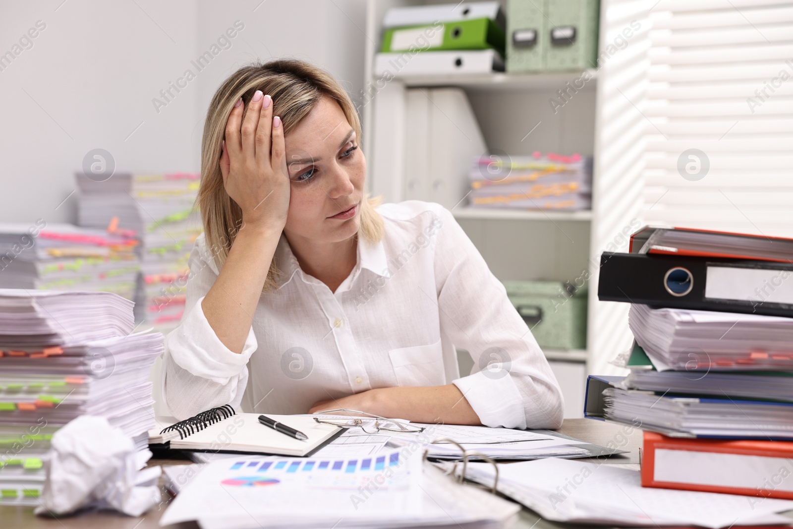 Photo of Overwhelmed woman surrounded by documents at workplace in office