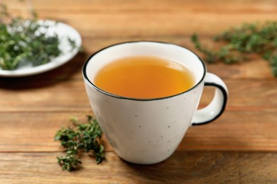 Photo of Aromatic herbal tea with thyme on wooden table, closeup