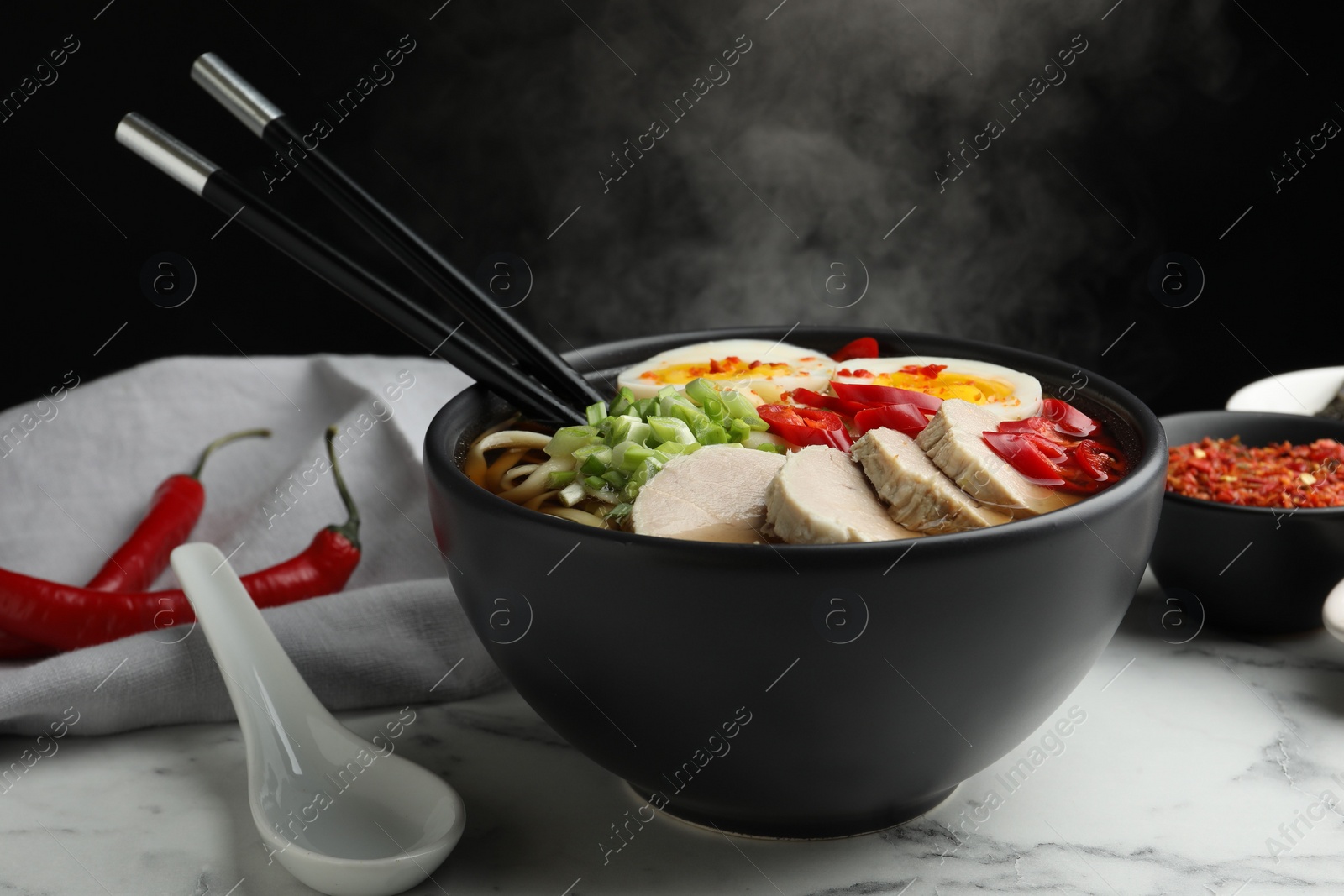 Photo of Delicious ramen in bowl on white marble table against black background, closeup. Noodle soup