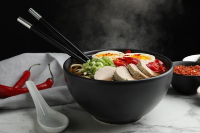 Delicious ramen in bowl on white marble table against black background, closeup. Noodle soup