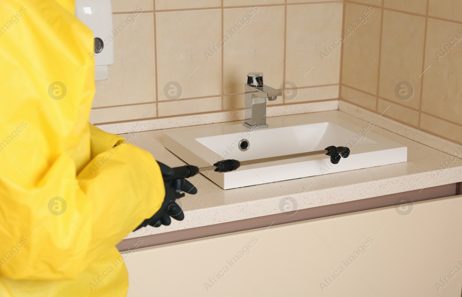Photo of Pest control worker spraying pesticide near sink in restroom, closeup