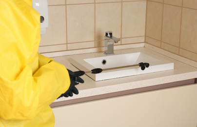 Photo of Pest control worker spraying pesticide near sink in restroom, closeup