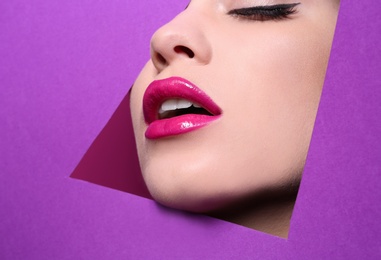 View of beautiful young woman with perfect lips makeup through cutout in color paper