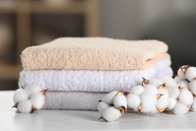 Photo of Terry towels and cotton branch with fluffy flowers on white wooden table in room, closeup