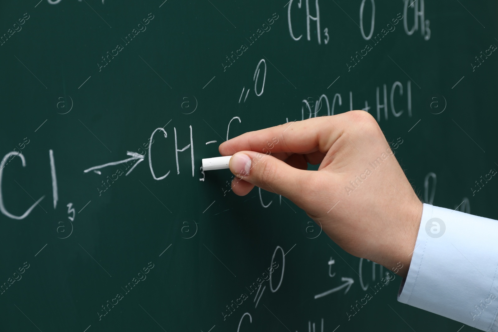 Photo of Teacher writing chemical formulas with chalk on green chalkboard, closeup