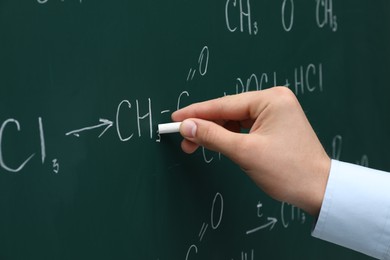 Photo of Teacher writing chemical formulas with chalk on green chalkboard, closeup