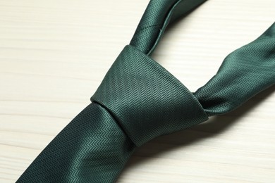 Photo of One green necktie on white wooden table, top view