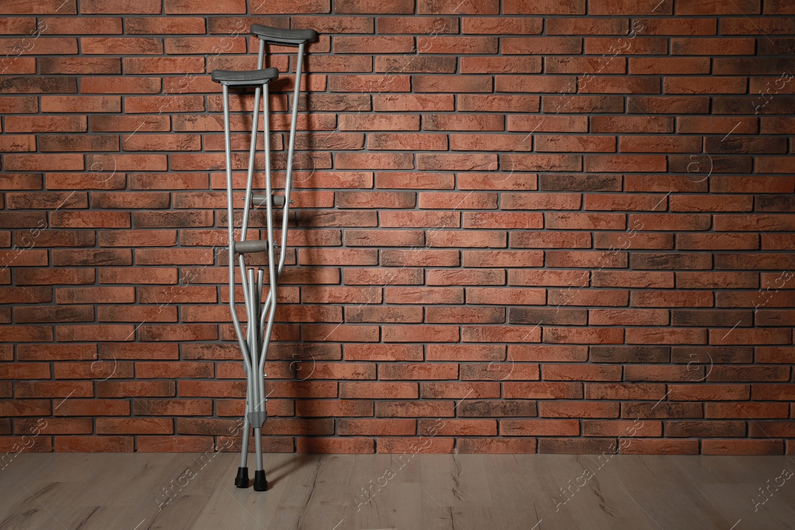 Photo of Pair of axillary crutches near red brick wall. Space for text