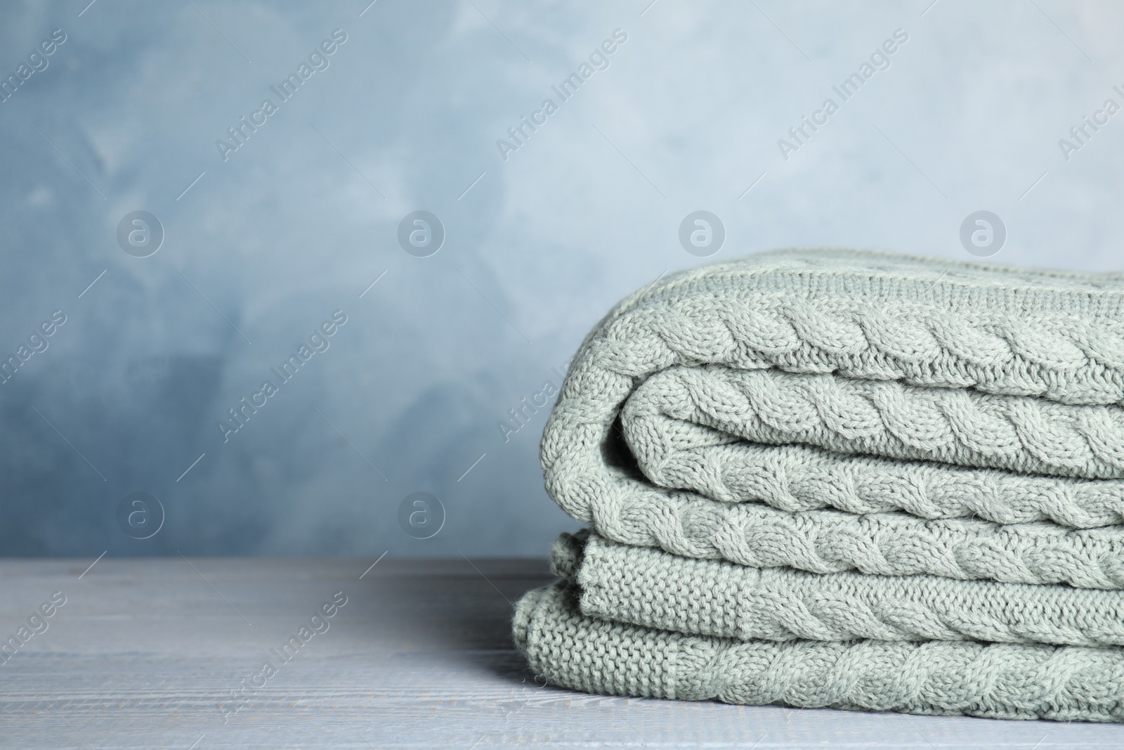 Photo of Knitted plaid on light grey wooden table, closeup. Space for text