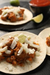 Photo of Delicious tacos with vegetables, meat and lime on dark table, closeup