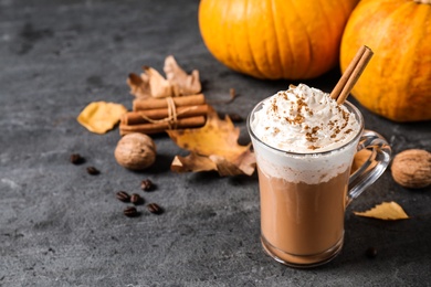 Photo of Pumpkin spice latte with whipped cream and cinnamon stick in glass cup on grey table. Space for text