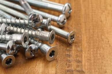 Many metal screws on wooden table, closeup. Space for text
