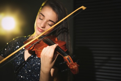 Photo of Beautiful young woman playing violin in dark room, focus on hand