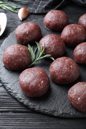 Photo of Many fresh raw meatballs on black wooden table