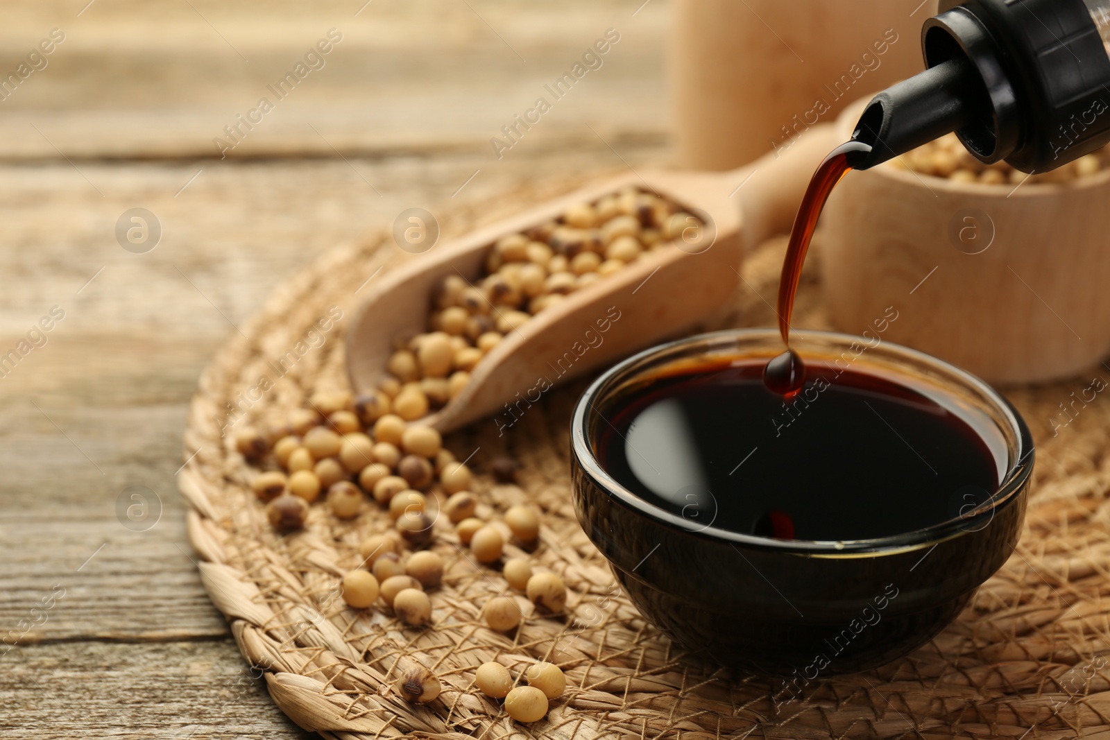 Photo of Pouring soy sauce into bowl at wooden table, closeup. Space for text