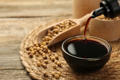 Photo of Pouring soy sauce into bowl at wooden table, closeup. Space for text