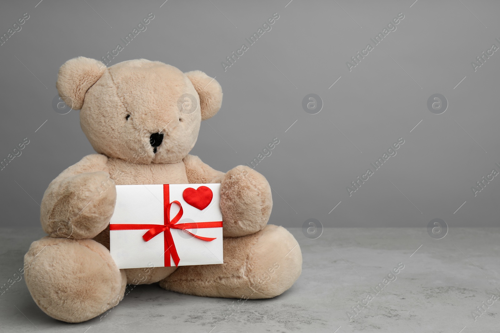 Photo of Cute teddy bear with envelope on light grey stone table, space for text. Valentine's day celebration