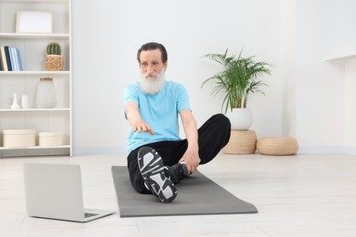 Photo of Senior man in sportswear stretching while watching online tutorial at home
